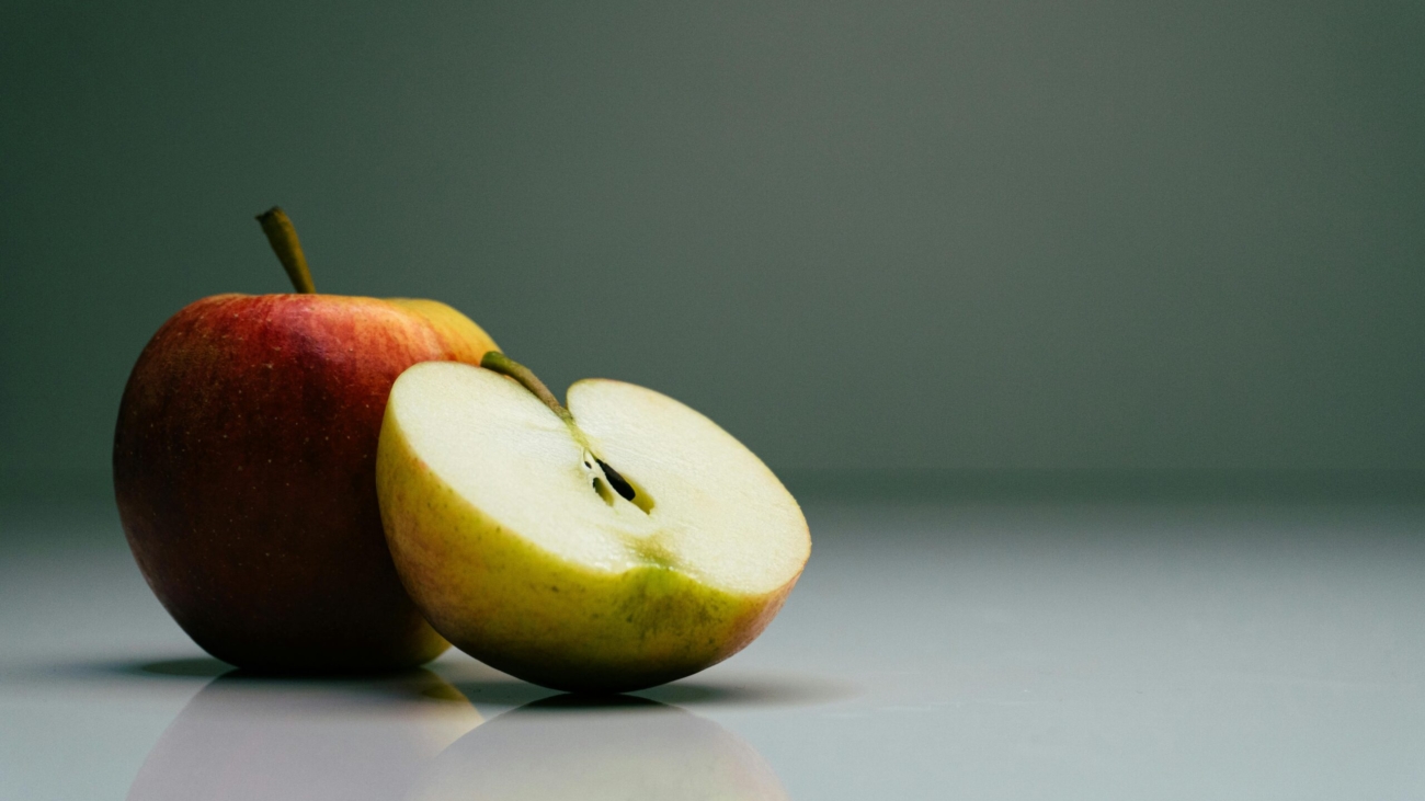 Close-up of a whole and sliced organic apple on a reflective surface.